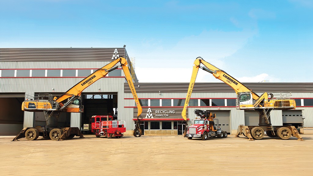 Two large material handlers and two large trucks in front of a recycling facility