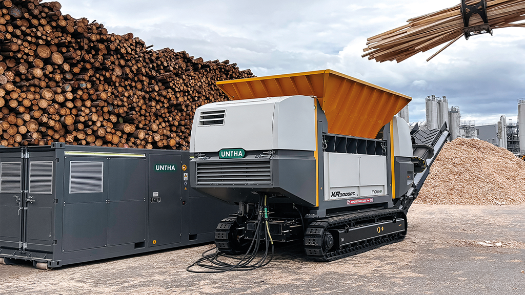 A semi-mobile wood shredder next to a large pile of wood waste