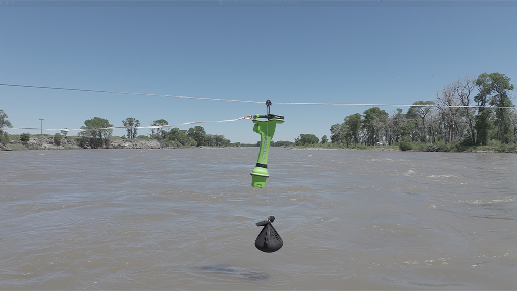 A small green device attached to a suspended wire over a river