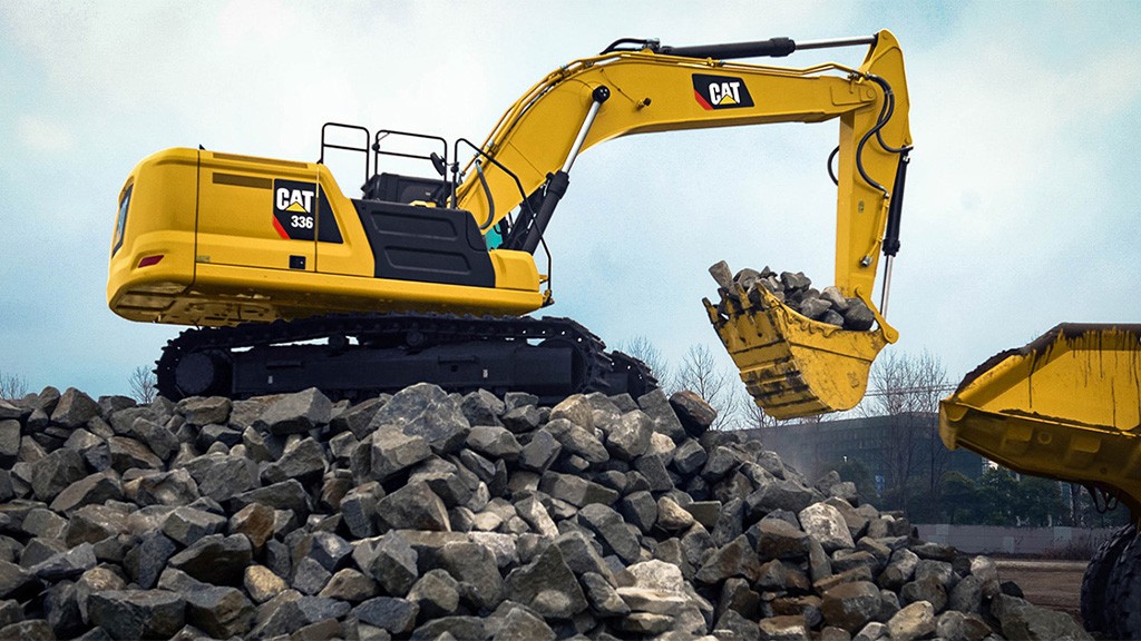 A Caterpillar excavator lifts a bucket filled with aggregates
