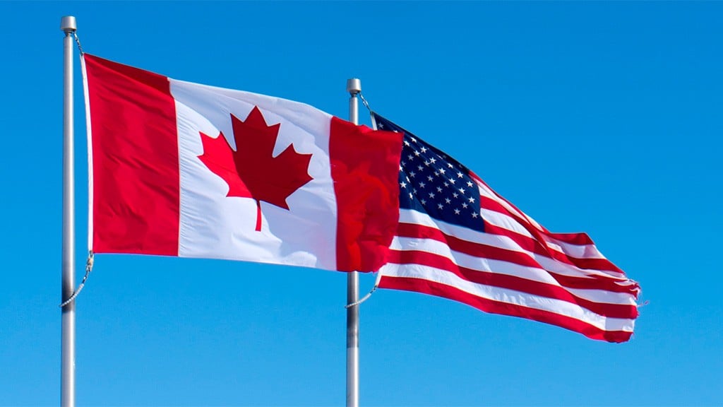 A Canadian and a United States flag wave in the wind A Canadian and a United States flag wave in the wind