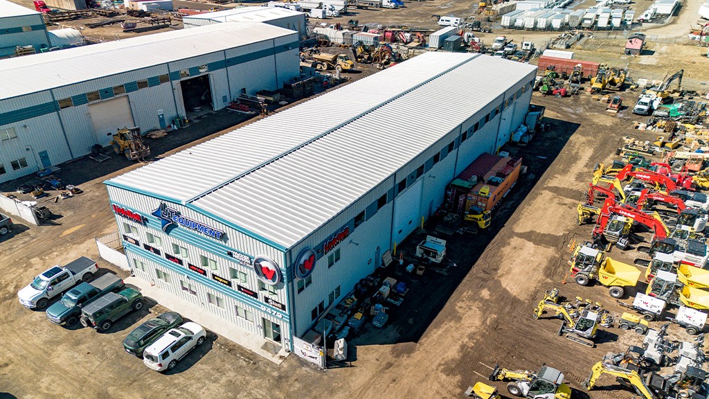 An aerial view of a large warehouse surrounded by cars and heavy equipment An aerial view of a large warehouse surrounded by cars and heavy equipment