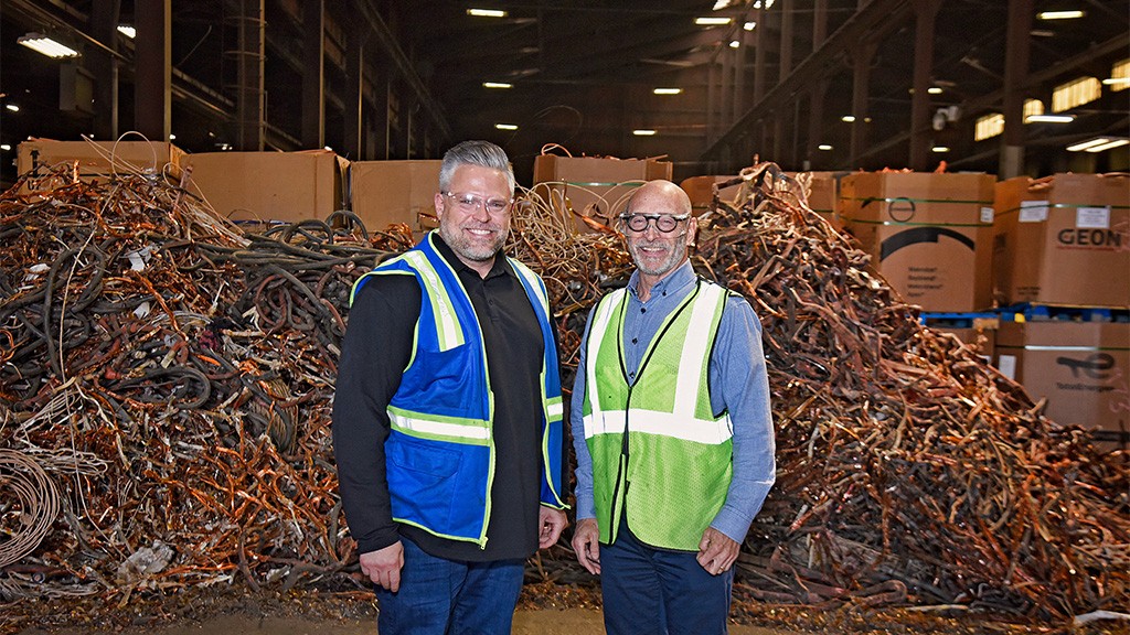 Two men pose for a photo in front of large bales of scrap copper Two men pose for a photo in front of large bales of scrap copper