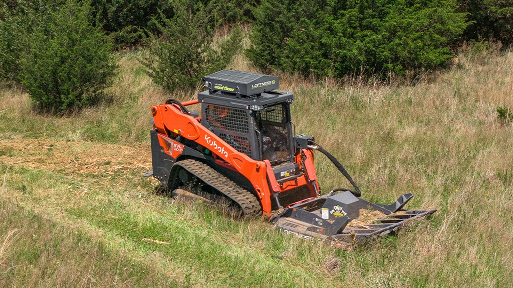 A Kubota skid steer loader fitted with a brush cutter attachment and a cooling mechanism on the roof