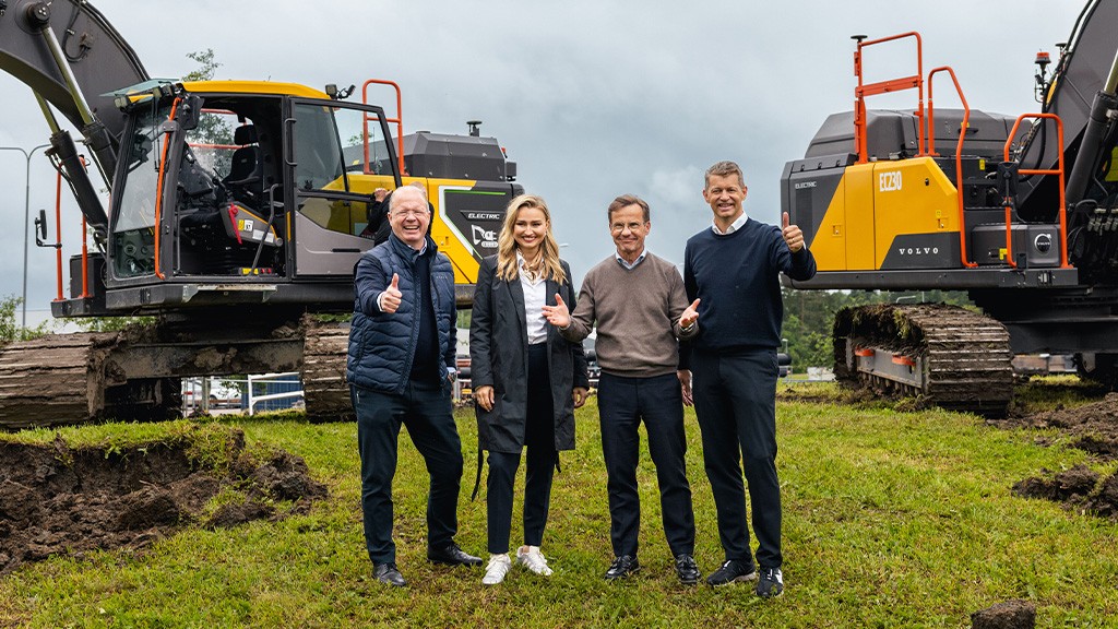 Four people stand in front of two crawler excavators Four people stand in front of two crawler excavators