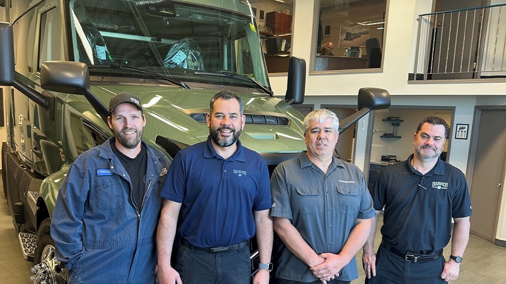 Four men pose for a photo in front of the cab of a vocational truck Four men pose for a photo in front of the cab of a vocational truck