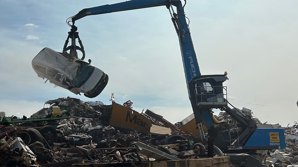 A material handler lifts a car in a metal scrap yard A material handler lifts a car in a metal scrap yard