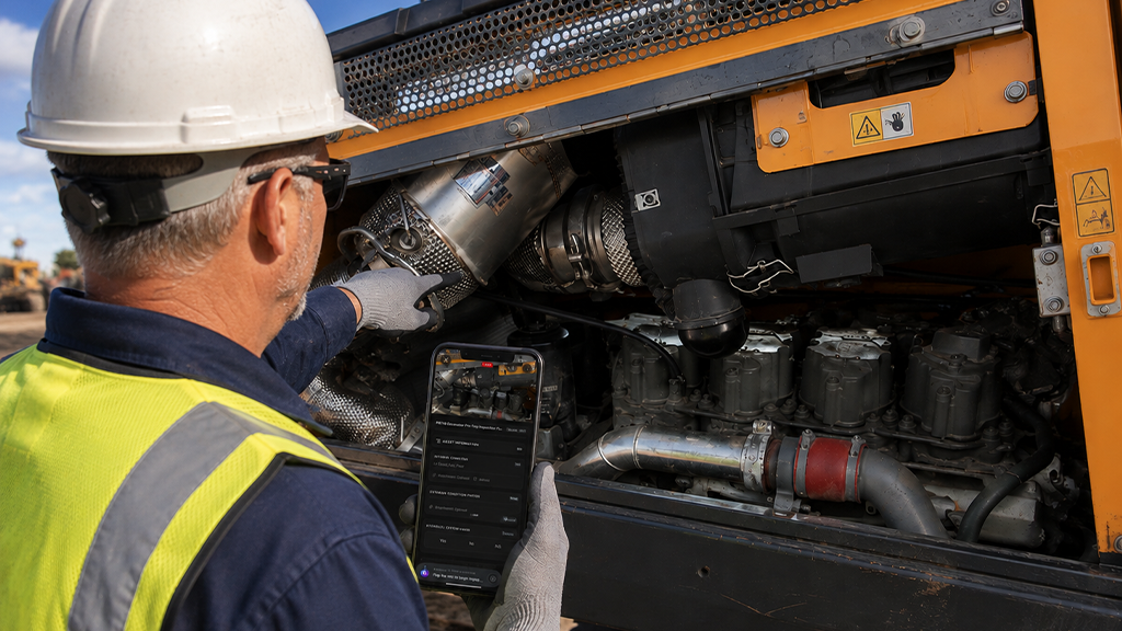 A man holds a smartphone while inspecting the engine of a piece of heavy equipment A man holds a smartphone while inspecting the engine of a piece of heavy equipment