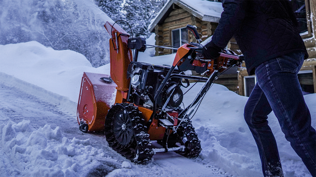 A man pushes a snow blower up a steep driveway A man pushes a snow blower up a steep driveway