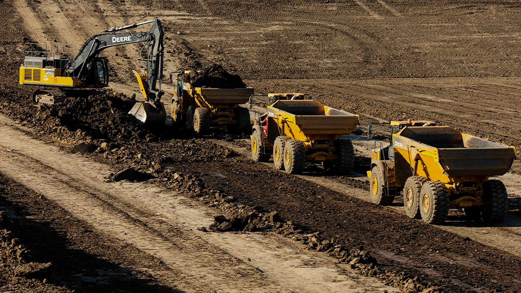 A fleet of haulers are loaded by an excavator on an outdoor site