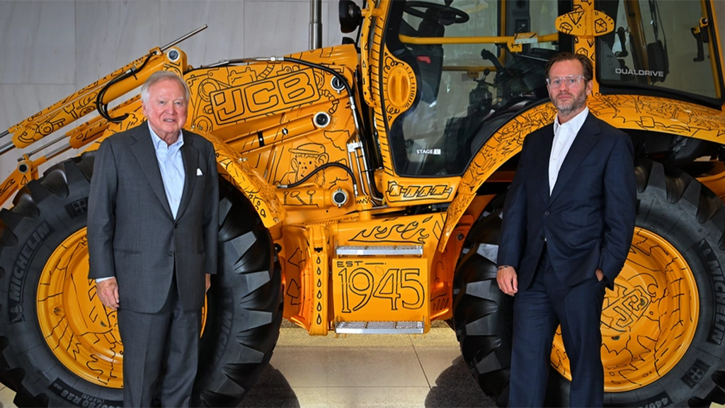 Two men pose for a photo in front of a backhoe loader Two men pose for a photo in front of a backhoe loader