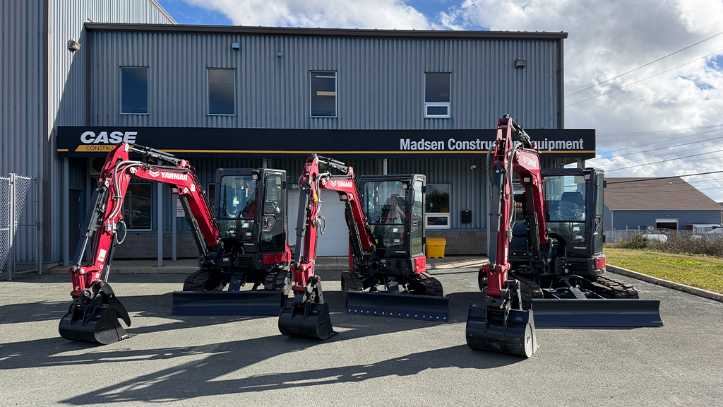Three excavators parked in front of a dealership