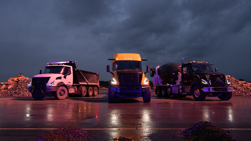Three vocational trucks lined up facing forward outdoors at night