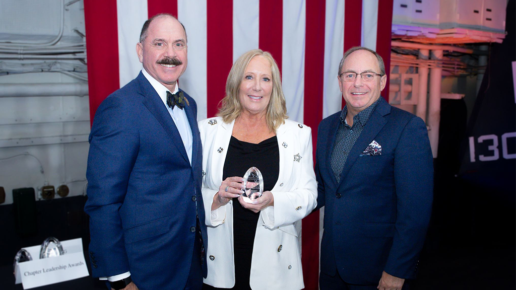Two men and one woman pose for a photo with a glass award Two men and one woman pose for a photo with a glass award