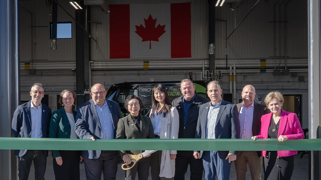 A team of people stand in front of a waste recycling facility ready to cut a large ribbon A team of people stand in front of a waste recycling facility ready to cut a large ribbon