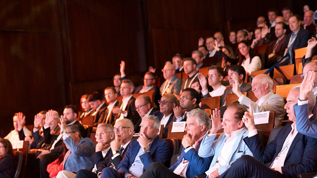 A crowd filled with people wearing business casual with some raising hands and others listening intently A crowd filled with people wearing business casual with some raising hands and others listening intently