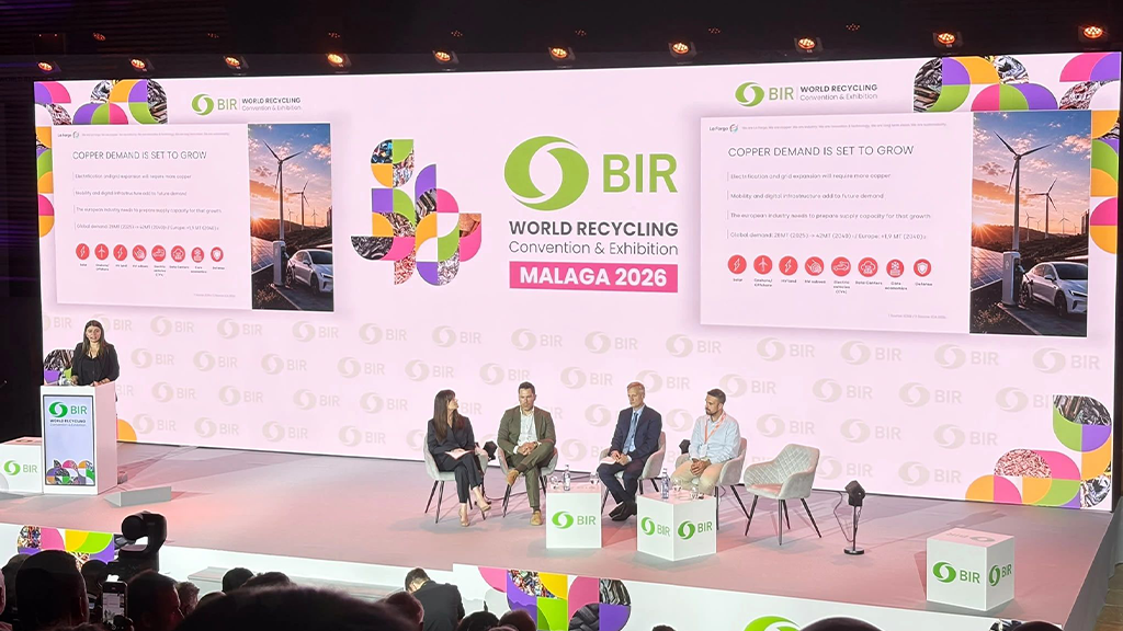 Four people sit in chairs on a stage with one person at a podium in front of BIR labelling Four people sit in chairs on a stage with one person at a podium in front of BIR labelling