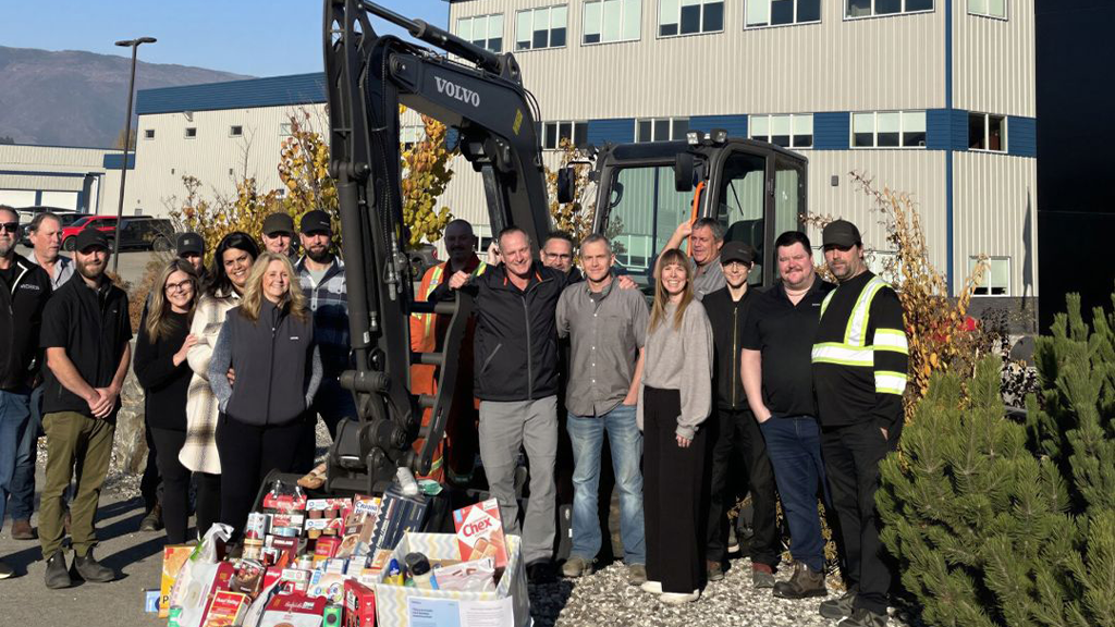 A group of people pose for a photo in front of a small excavator
